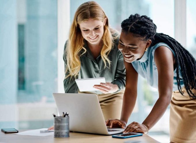 Two diverse businesswomen working together on a digital tablet and laptop in an office